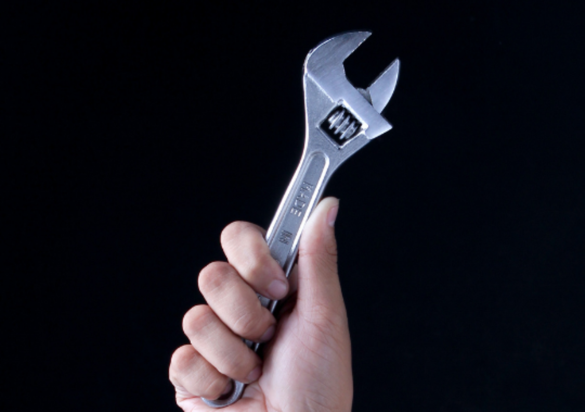 Image of hand holding a wrench for property repairs against a black background
